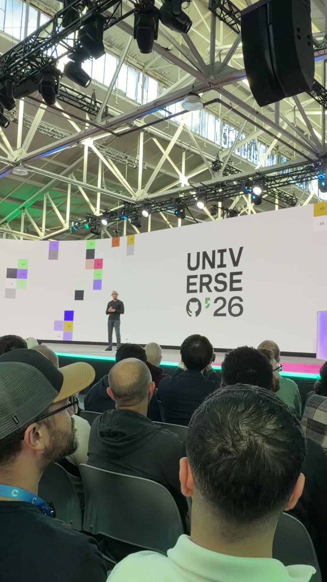 The GitHub Universe ’26 keynote stage, with a speaker, colorful pixel graphics, and the audience in the foreground.
